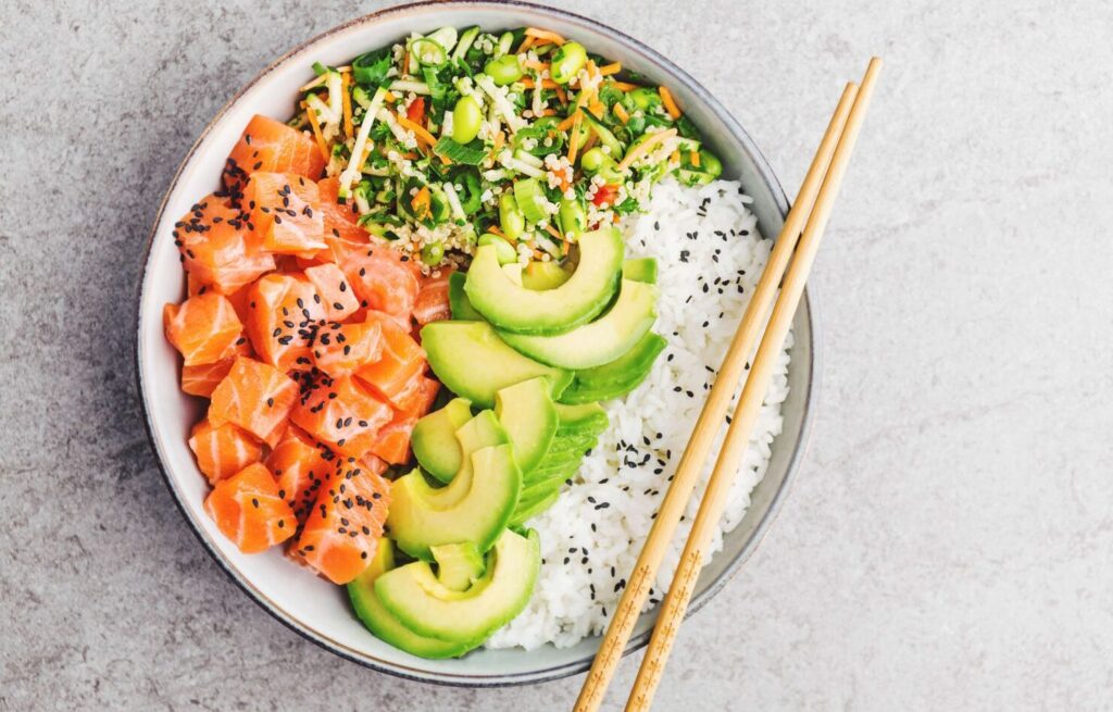 Ingredientes frescos para poke bowl: salmón, aguacate, arroz, pepino, zanahoria, sésamo.